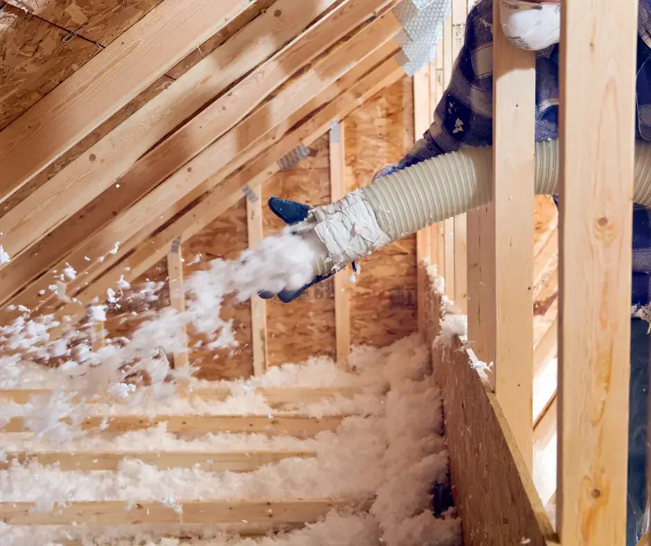 Technician using a hose to spray blown-in cellulose insulation into an attic space in a Virginia Beach home