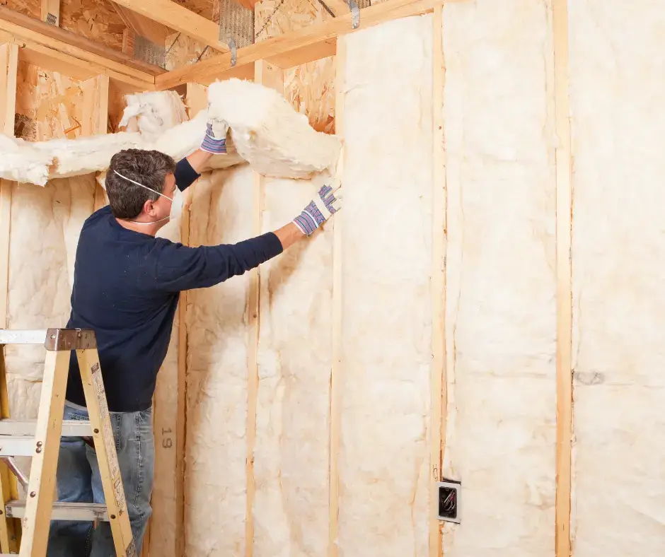 Technician on a ladder installing fiberglass batt insulation into wall stud cavities in a Virginia Beach home