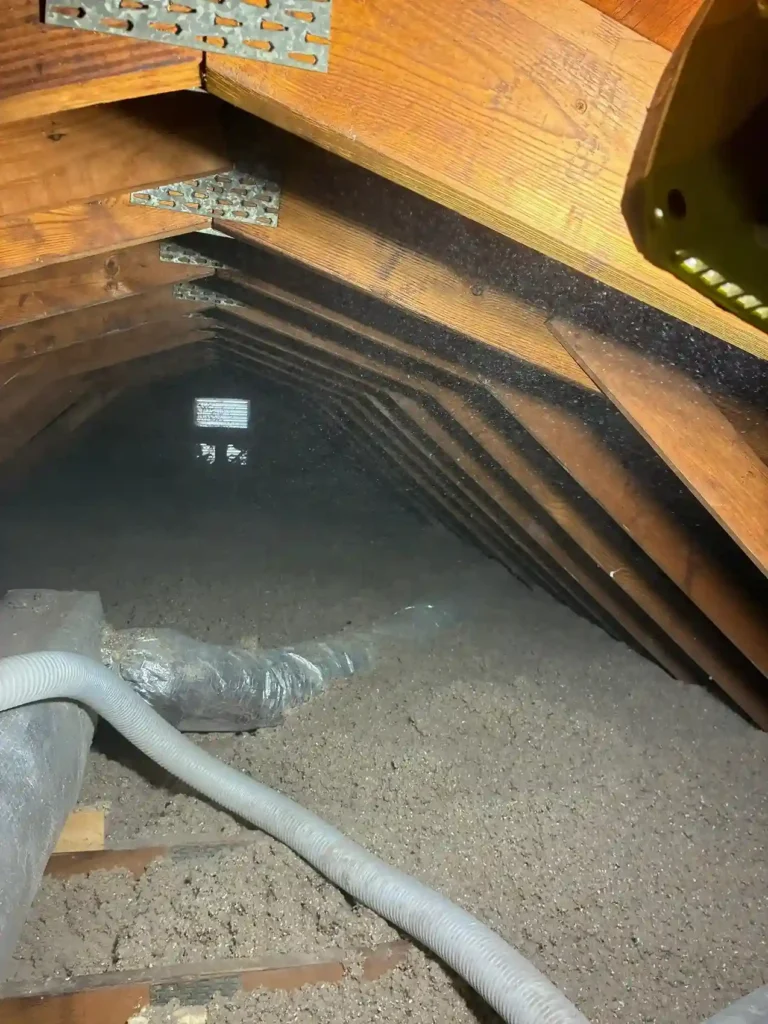 Blown-in cellulose insulation covering attic floor with flexible ductwork and gable vent in a Hampton Roads home by Level Home Pros